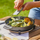 Person using Ooni Cast Iron Skillet while grating cheese