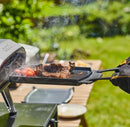 Person grilling meat on a portable grill outdoors using Ooni Dual Sided Grizzler Plate